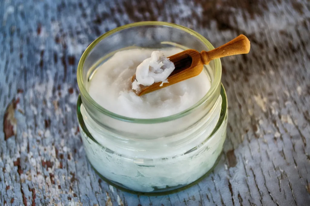 Jar of coconut oil with wooden scoop used for natural skin moisturizing