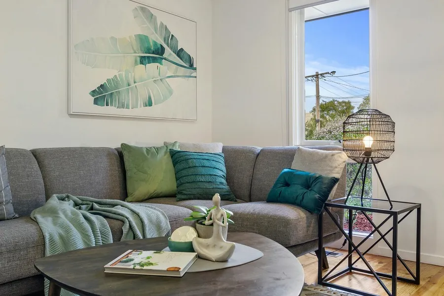 Cheap decor ideas in a bright living room with green cushions, a throw blanket, framed leaf wall art and a wire pendant lamp