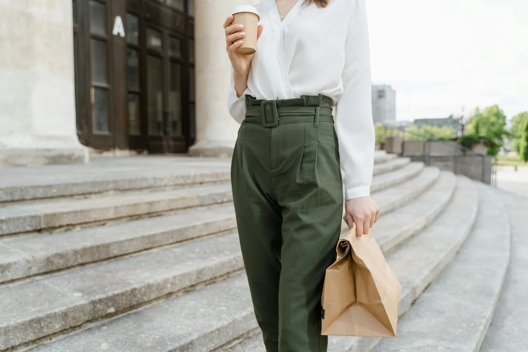 Busy professional woman holding a coffee cup and takeaway lunch while walking down outdoor steps