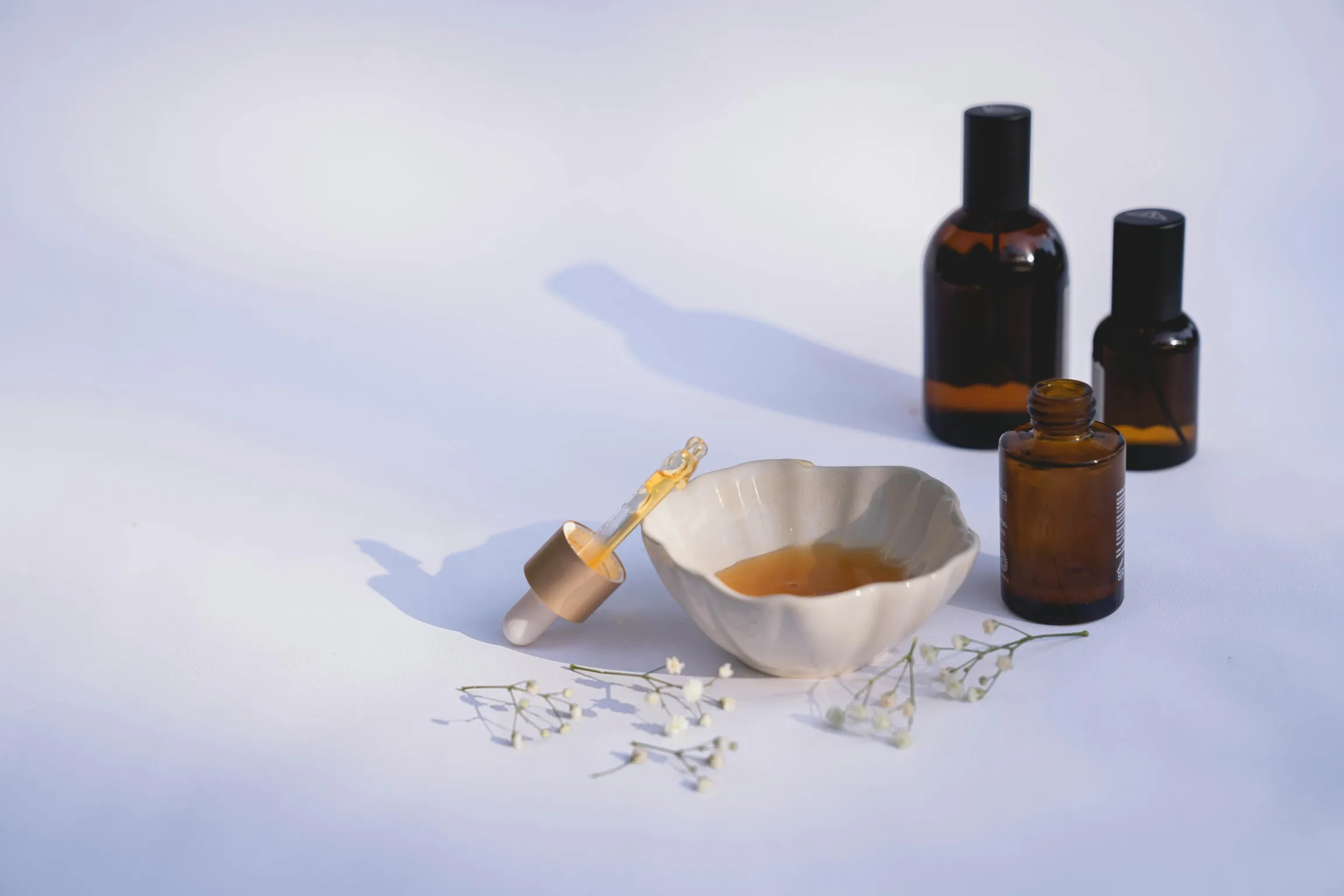 Bottles of hair oil with a dropper and small bowl on a white surface