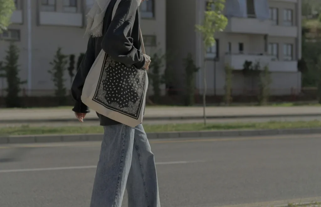 Person wearing casual streetwear and carrying a patterned tote bag on a city street, reflecting tote bag culture