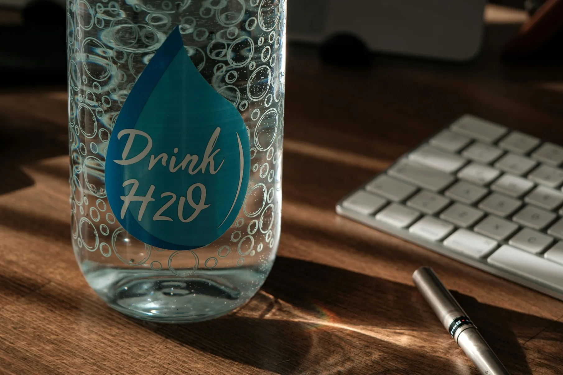 Water bottle on a desk next to a keyboard and pen.