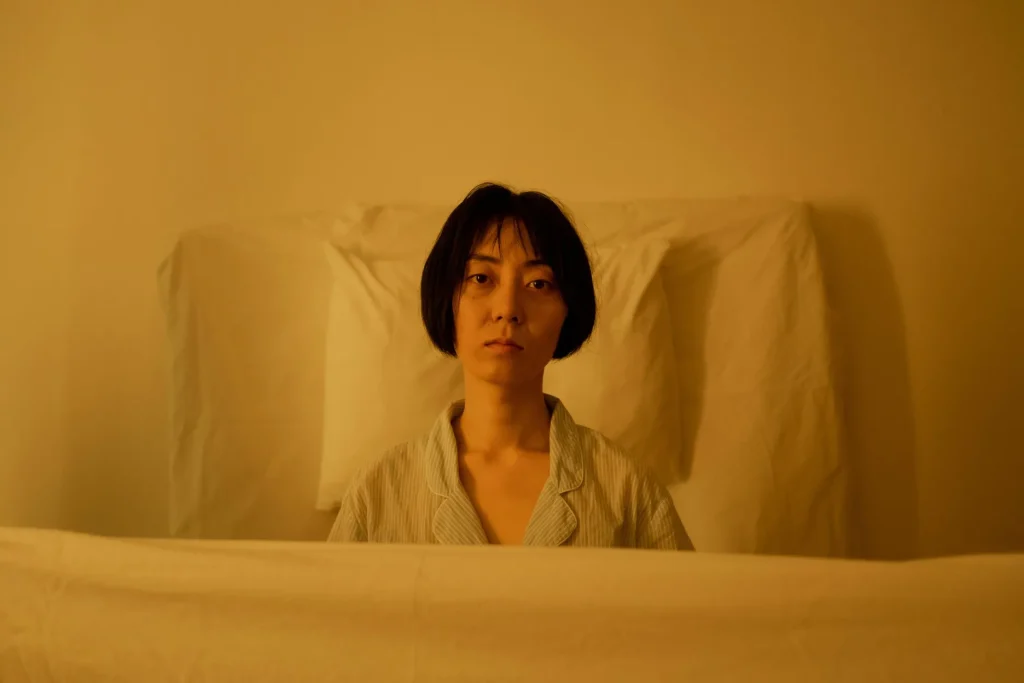 Woman lying awake in bed under warm yellow light, looking tired and exhausted