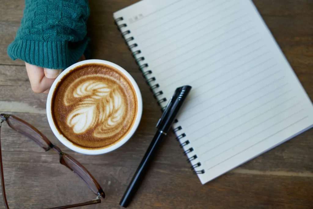 Woman journaling at her desk, with a notebook and a cup of coffee nearby.