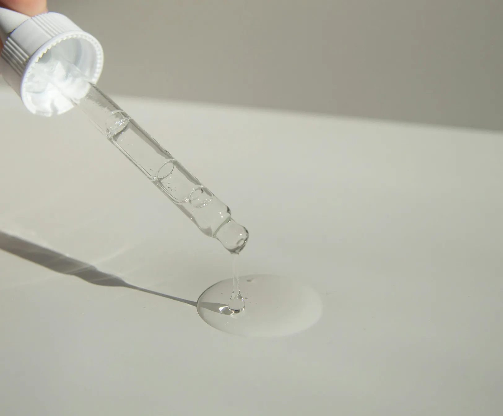 Close-up of a clear niacinamide serum dropper releasing product onto a white surface..